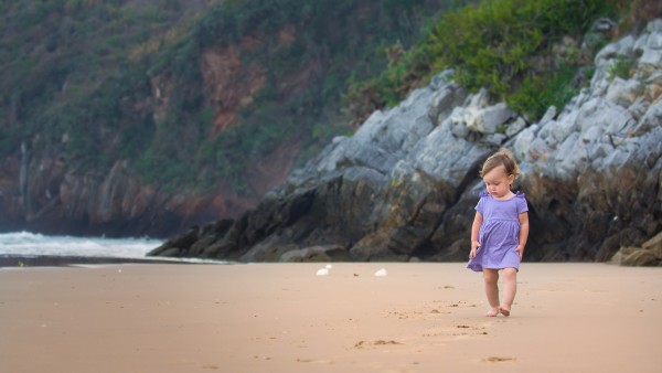 Маленькая девочка гуляет босиком по песчаной набережной