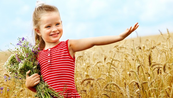 Милая маленькая девочка в пшеничном поле с букетом цветов