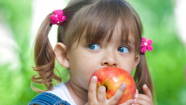 Девочка с голубыми глазами кушает красное яблоко