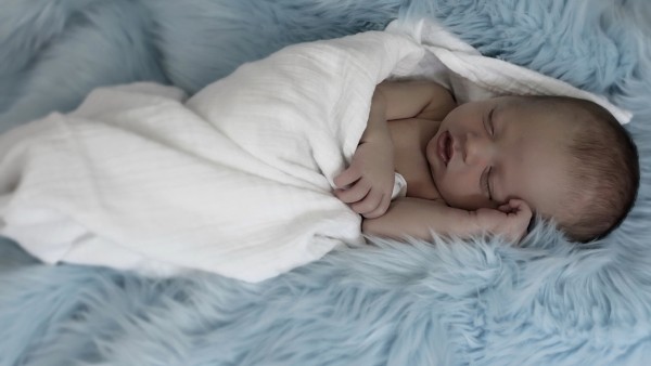 Новорожденный малыш спит укутавшись на пушистой кровати