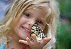 Маленькая улыбающаяся девочка держит в руках бабочку