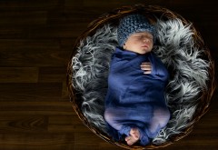 Маленький младенец в шапке спит в корзине